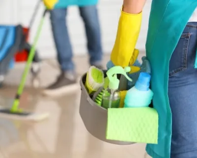 A cleaner entering a home with a box of cleaning supplies.